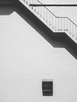 Black and white photo of a modern building's exterior staircase with strong shadows.